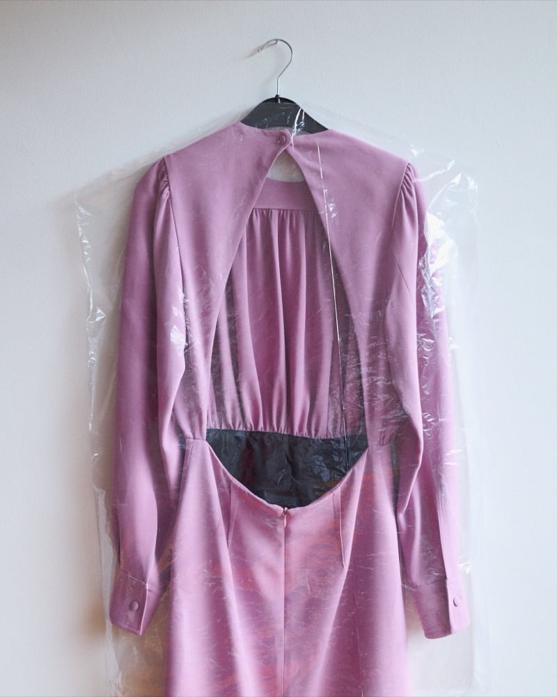 A mauve satin KRISVANASSCHE dress with a gathered waist hanging inside a clear garment bag