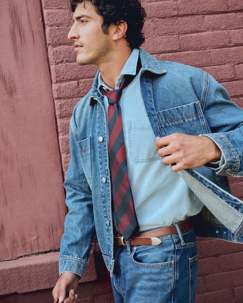 Raphael Diogo adjusting his denim jacket lapel over a striped tie