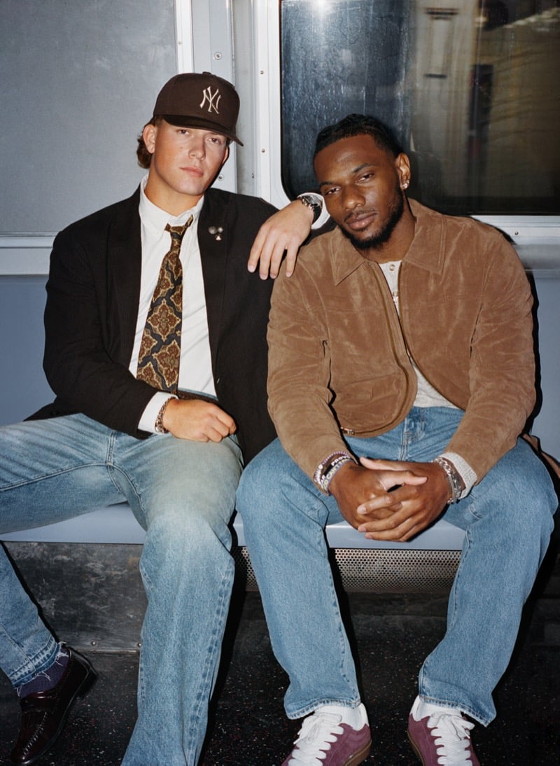 Jaxson Dart and Malik Nabers sit side by side on a subway bench wearing a blazer and a suede jacket with straight-leg jeans and sneakers