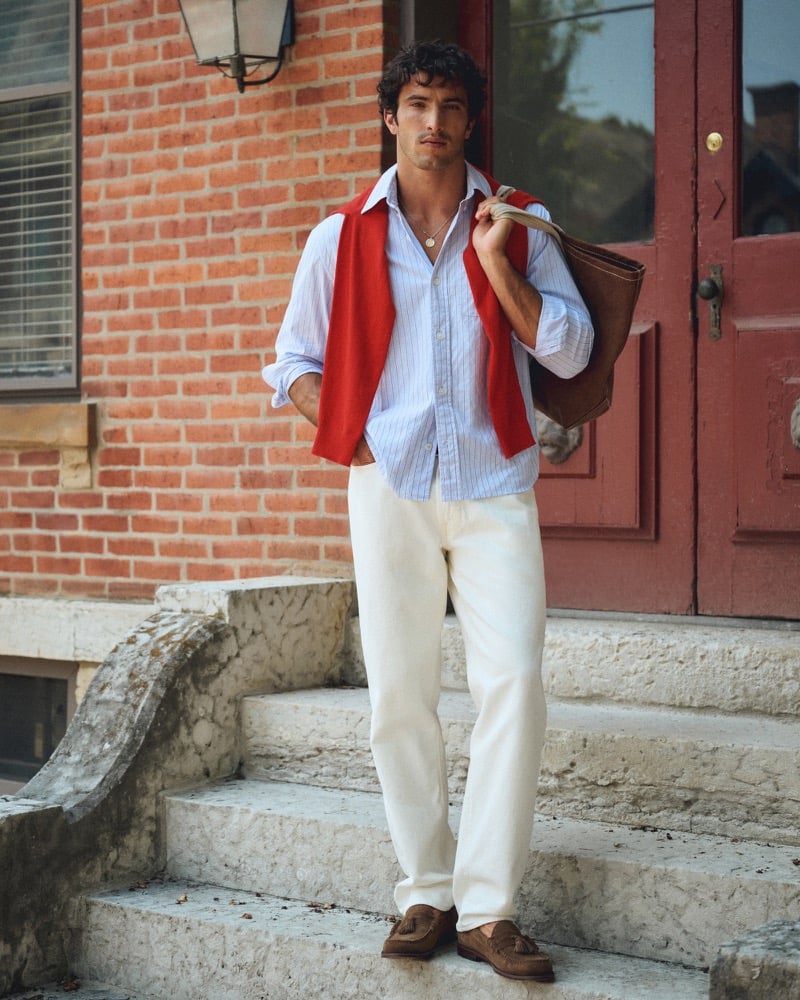Raphael Diogo in a striped shirt with a red sweater draped over his shoulders and white wash jeans