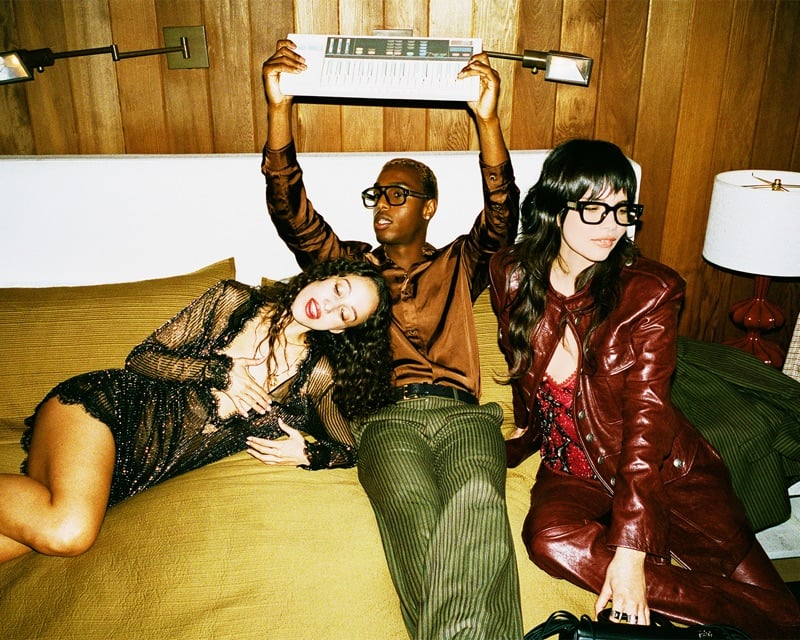 Jade Croonenberghs, Bakar, and Bianca Lexis lounge on a bed as Bakar lifts a synthesizer overhead for AMIRI's fall-winter 2026 campaign