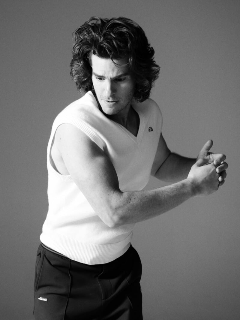 Andrew Garfield wears a white knit V-neck vest in a black-and-white image for ellesse's 2026 campaign