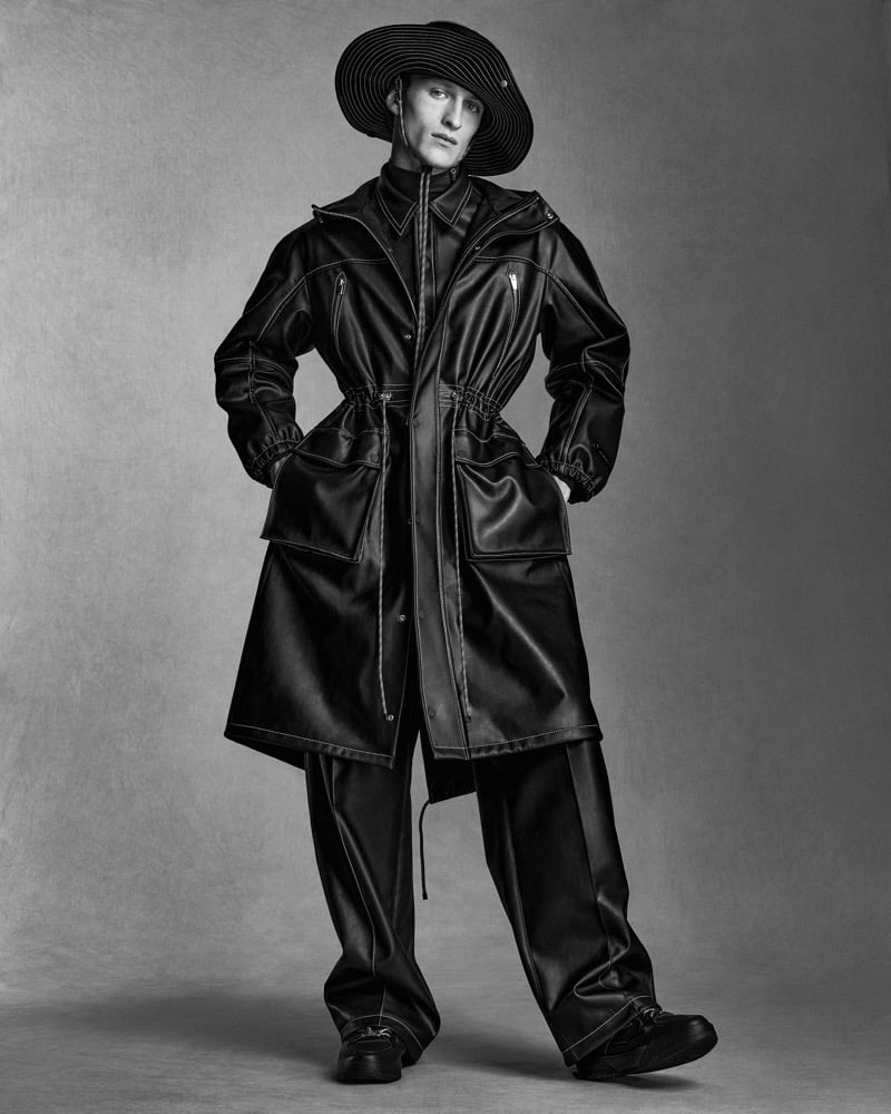 Vasko Luyckx wears a topstitched leather drawstring parka, wide trousers, and a wide-brim ridged hat for ANTAZERO season one, photographed in black and white