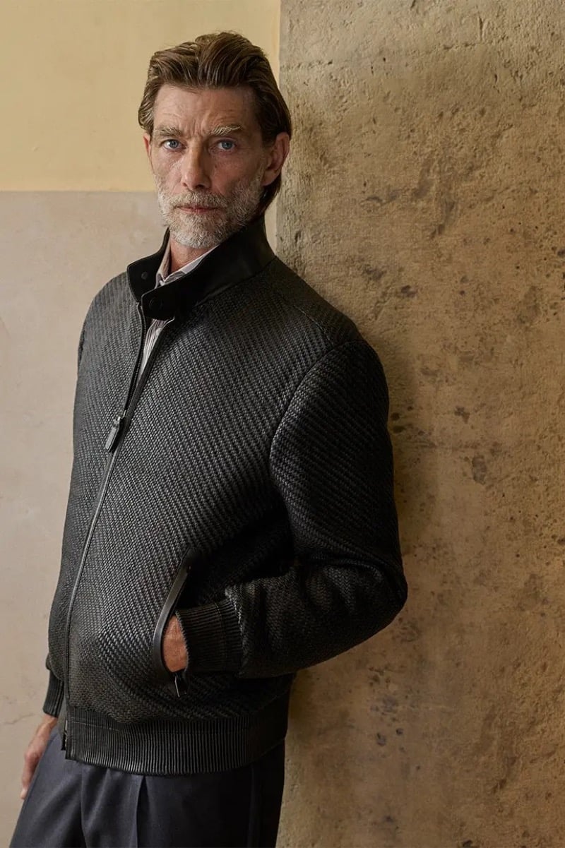 Patrick Petitjean leans against a stone column in a woven leather bomber jacket with a leather stand collar for Brioni's fall-winter 2026 campaign