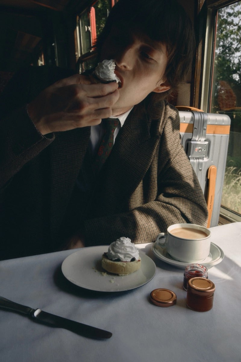 Erik Kettschik eats a cream-topped scone at a table set with tea and jam aboard the train for Carl Friedrik's fall 2026 campaign