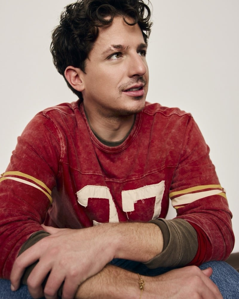 Charlie Puth sits in a faded red football jersey numbered 37, glancing off to the side