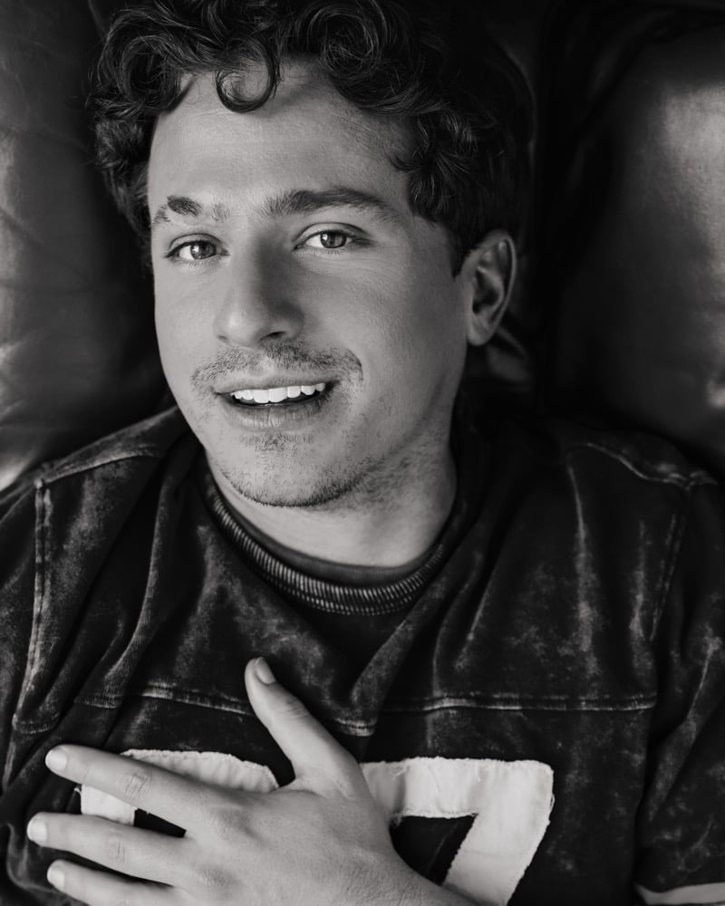 Black-and-white image of Charlie Puth lying back and smiling in a football jersey, hand on his chest