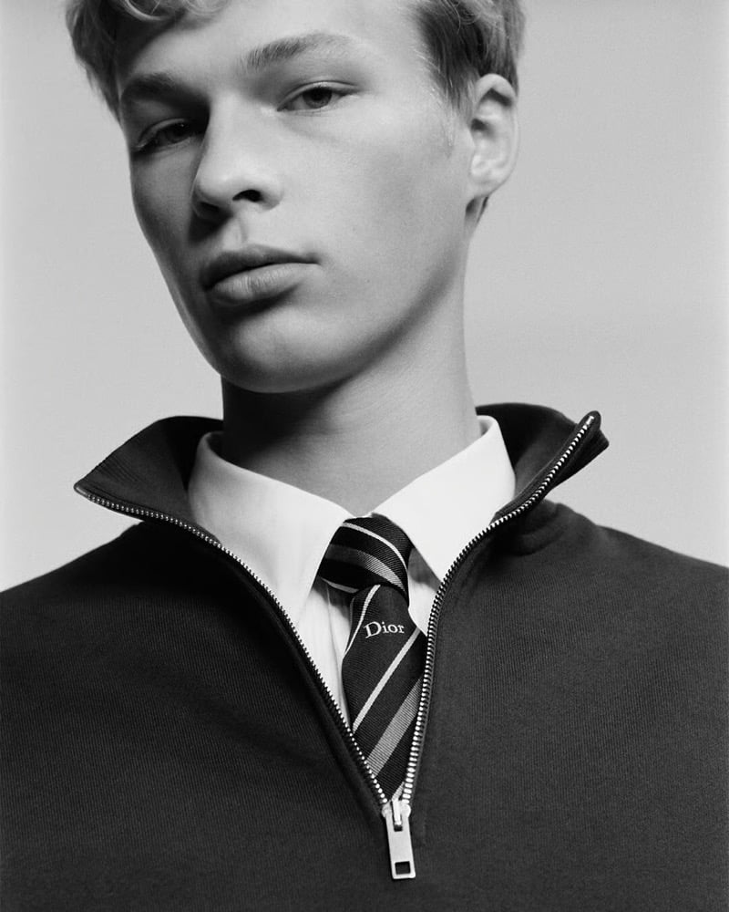Close-up of a striped Dior tie tucked into a black zip sweater over a white shirt collar