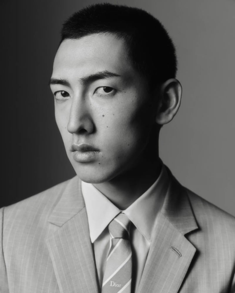 Close-up portrait of a model in a pinstripe suit and striped Dior tie against a gray backdrop