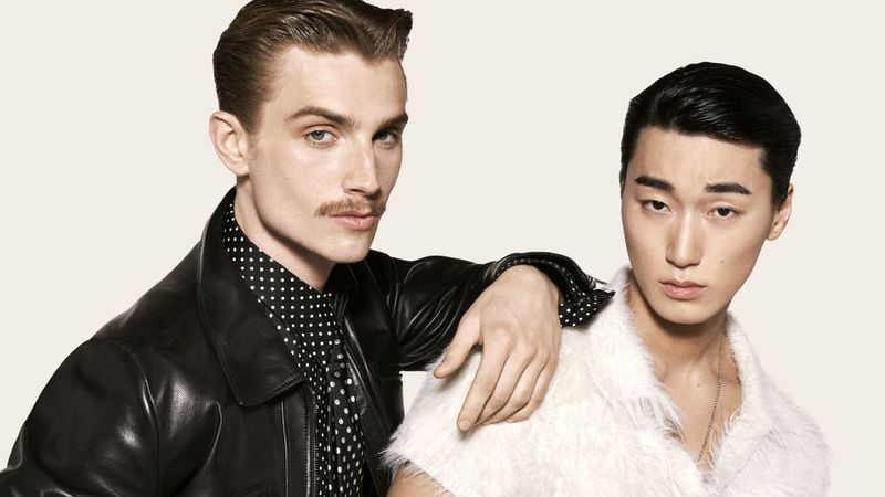 Ruben Aiello in a leather jacket and polka-dot scarf leans on San, who wears a shaggy knit top and pendant necklace
