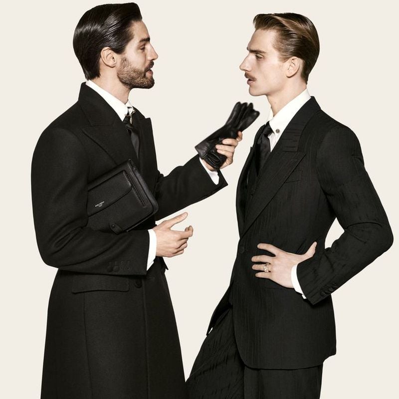Kilian Zeugin and Ruben Aiello stand face to face in profile, one holding leather gloves and a clutch bag