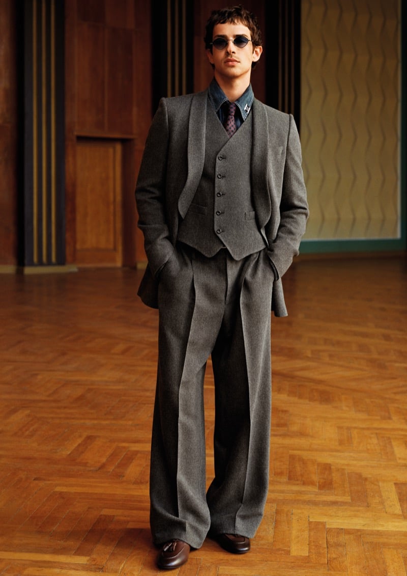 Manu Ríos in a gray three-piece suit over a denim shirt and patterned tie with oval sunglasses for Emporio Armani's fall-winter 2026 campaign