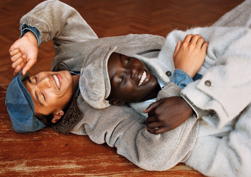 Morgan Sahadow and Josephen Akuei lie tangled on a parquet floor, laughing, in denim shirts and textured wool coats for Emporio Armani's fall-winter 2026 campaign