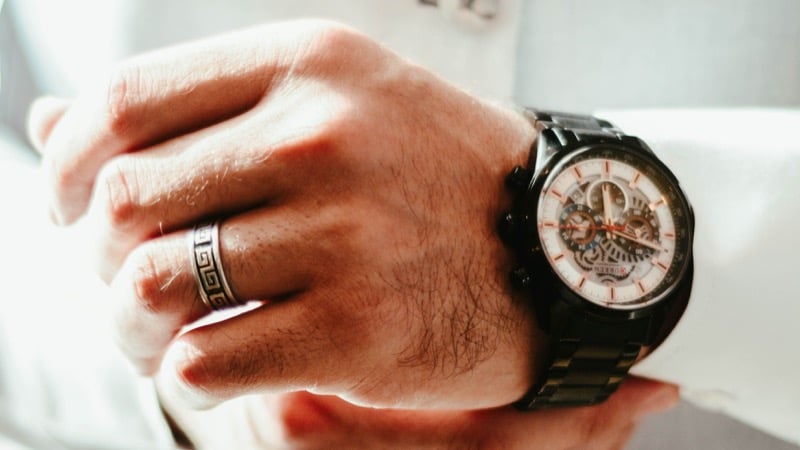 A man's hand wearing an engraved wedding band alongside a watch