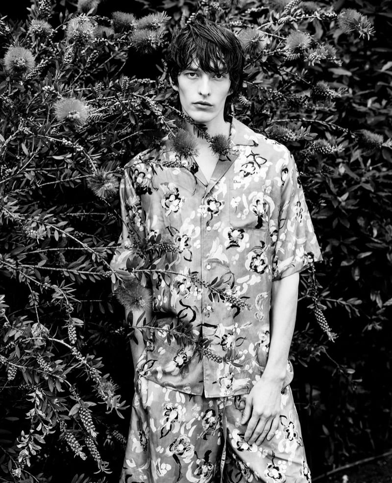 Erik Kettschick poses among flowering branches in a black-and-white portrait, wearing a floral-print shirt and matching shorts