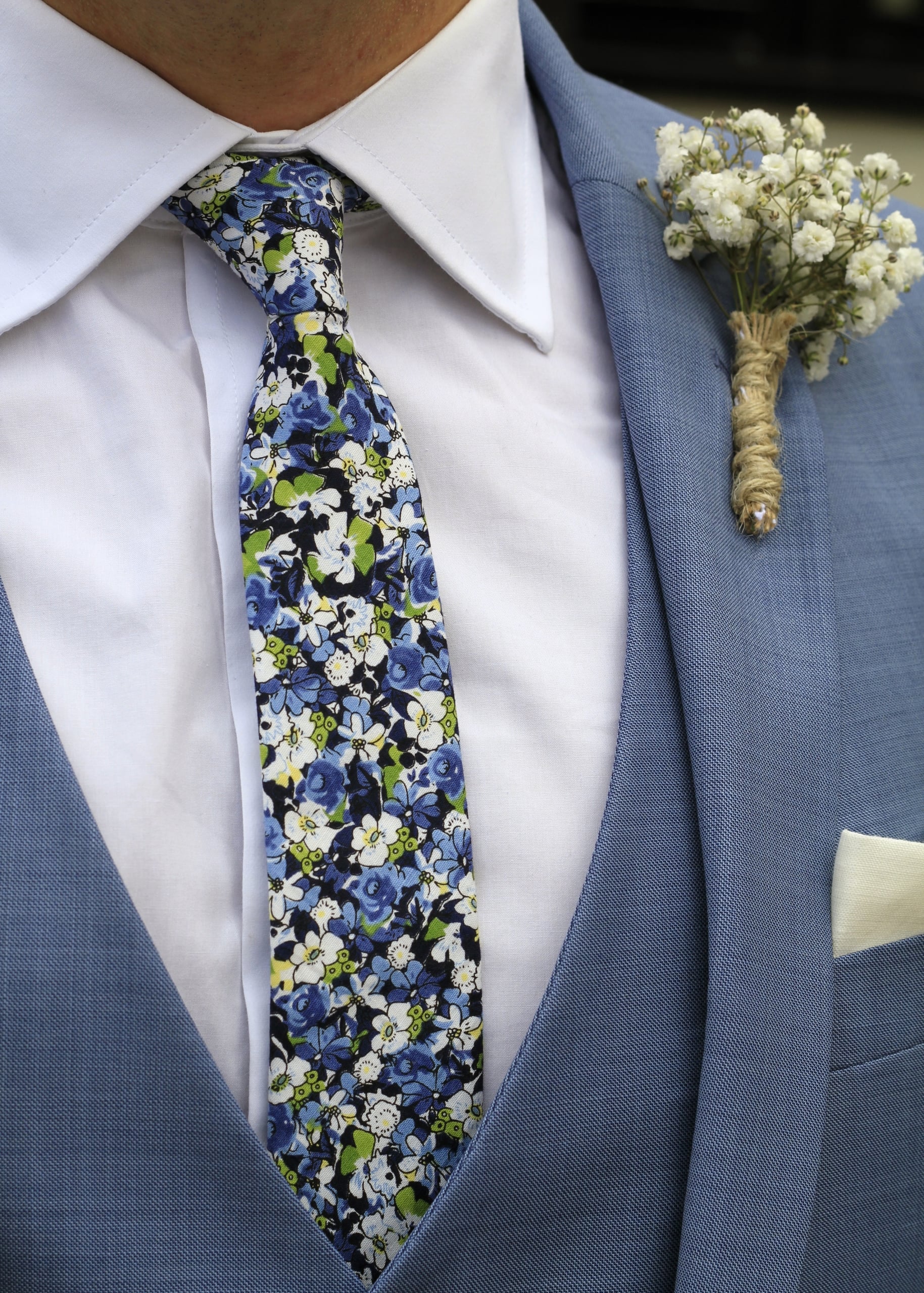 A close-up of a man in a light blue three-piece suit wearing a dense blue and green floral tie