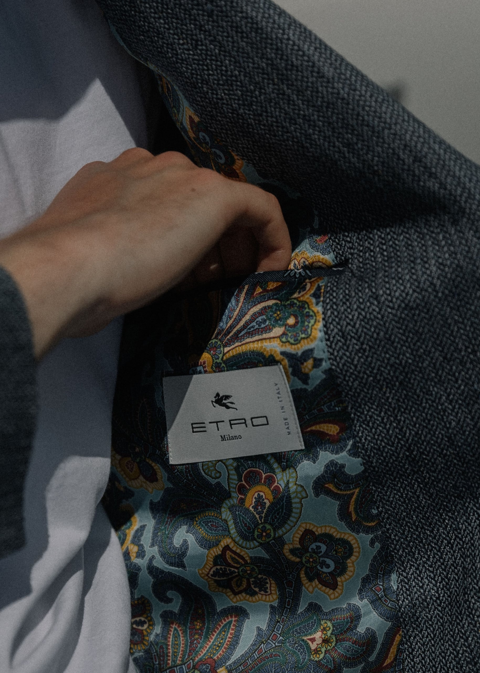 A hand pulls back the lapel of a gray jacket to reveal an Etro paisley floral silk lining