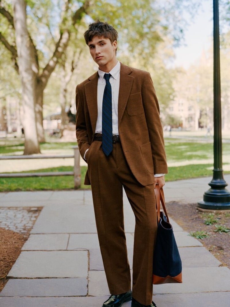 Jack Lumsden in a brown suit and striped tie carrying a tote bag on the Yale campus