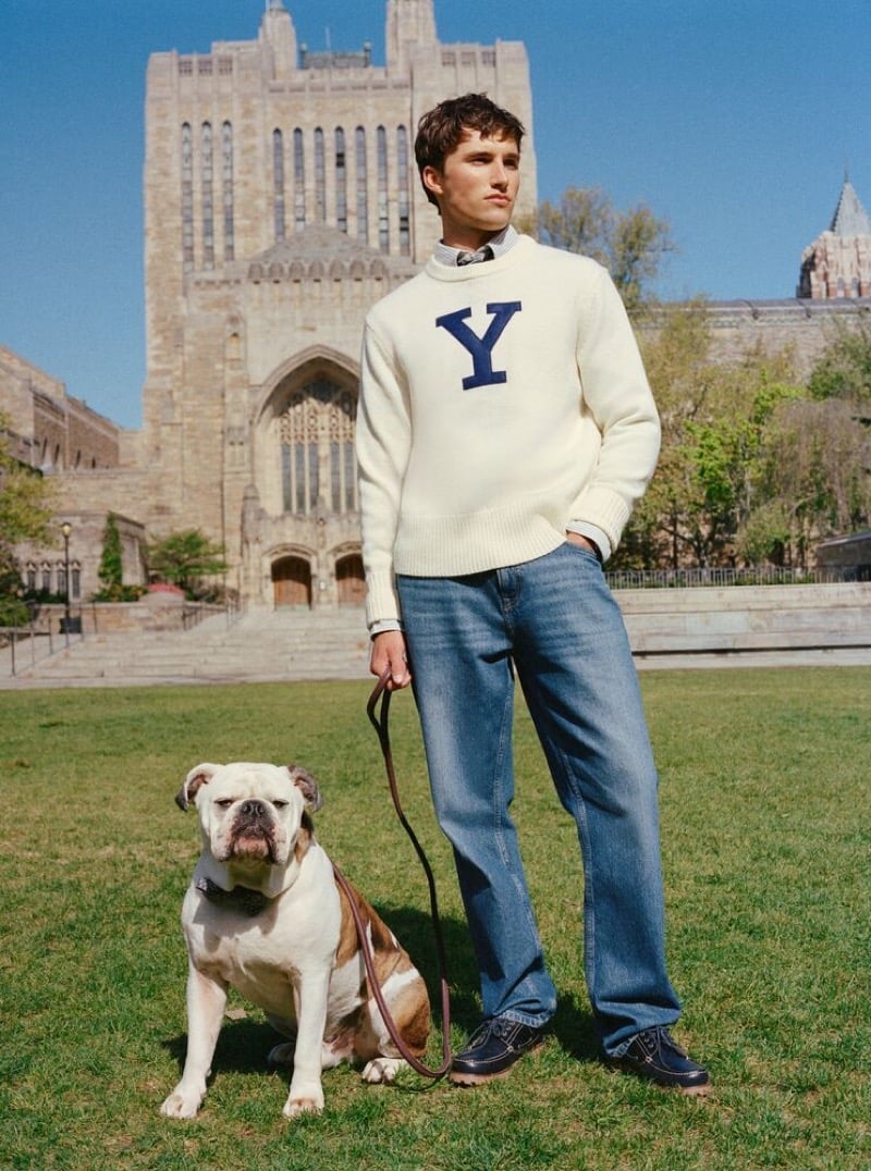 Jack Lumsden in an ivory letter sweater walking a bulldog in front of Sterling Memorial Library