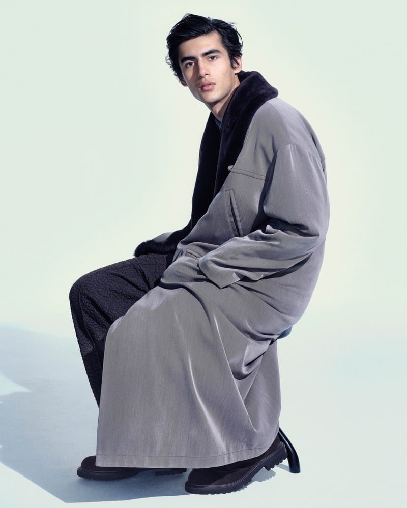 Akbar Shamji sits wearing a floor-length gray fur-lined coat with lug-sole boots for Giorgio Armani's fall-winter 2026 campaign