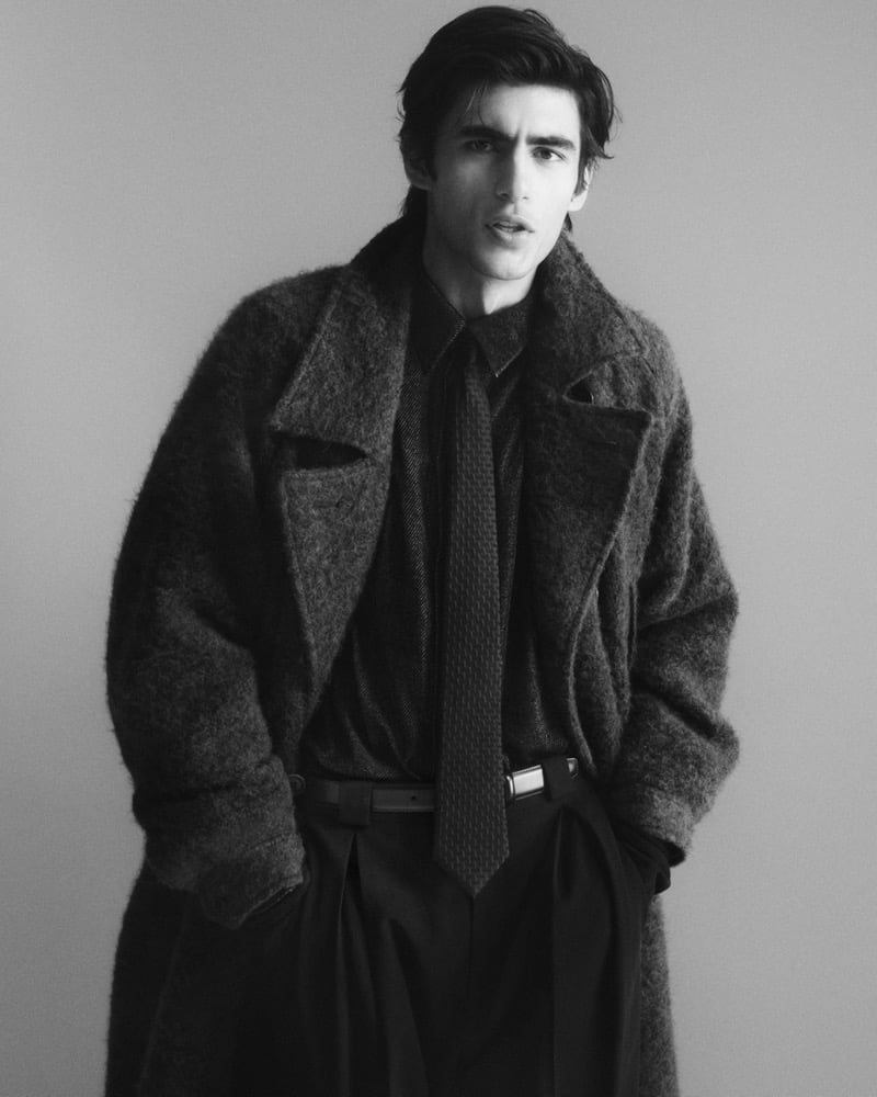 Akbar Shamji wears an oversized brushed wool overcoat over a dark shirt and tie with pleated trousers in a black-and-white image for Giorgio Armani's fall-winter 2026 campaign