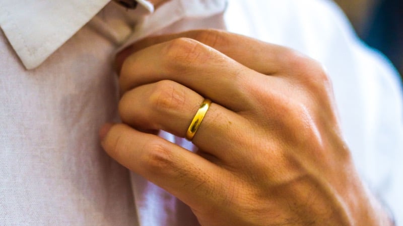 A man's hand at his shirt collar wearing a polished gold wedding band