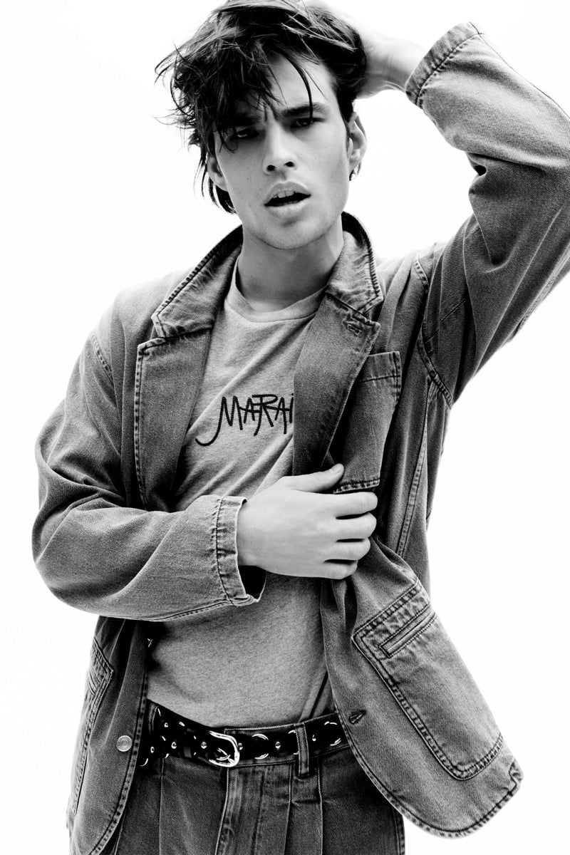 Louis Baines in a black-and-white image wears a washed jacket over a logo T-shirt with a studded belt, for Isabel Marant Fall 2026