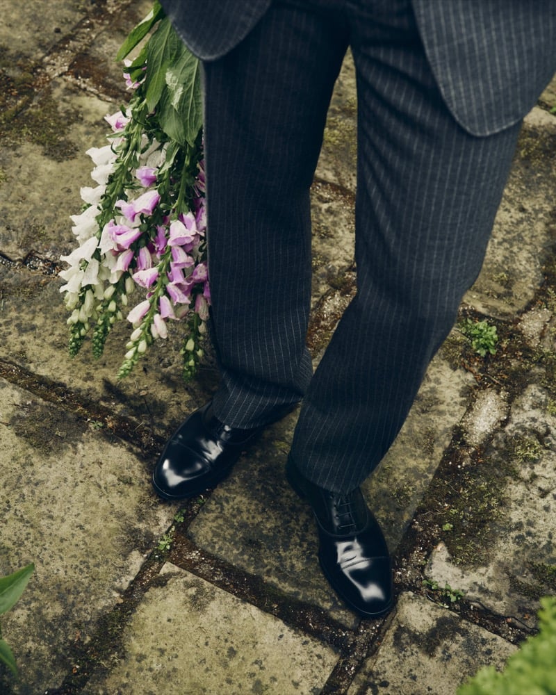 Close-up of polished black lace-up shoes and pinstripe trousers beside a bouquet of pink and white flowers