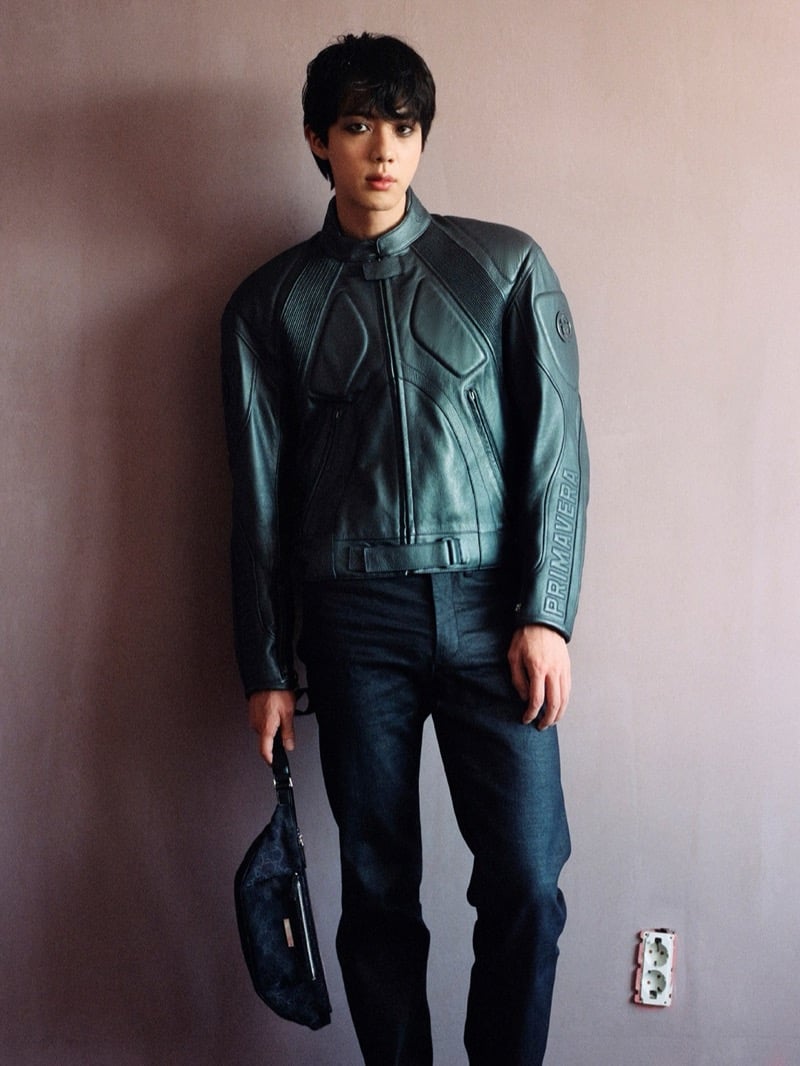 Jin wears a racing-style leather jacket embossed with Primavera down the sleeve, holding a GG monogram bag for Gucci's Primavera campaign