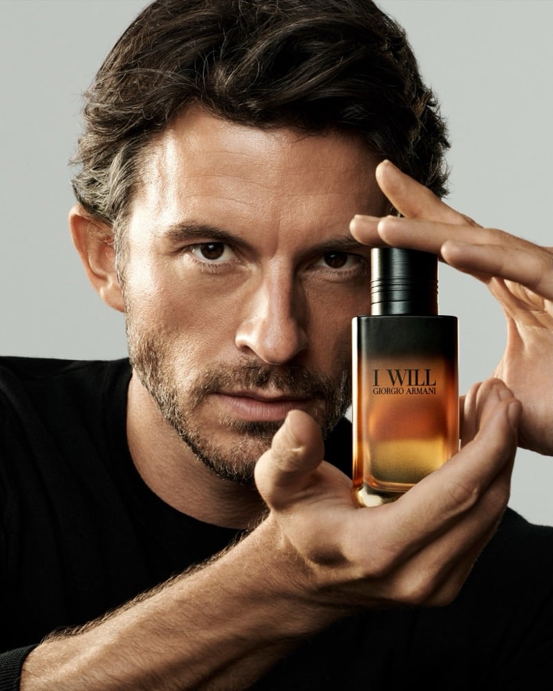 Jonathan Bailey in a black T-shirt holding the Giorgio Armani I Will bottle up to frame his eye