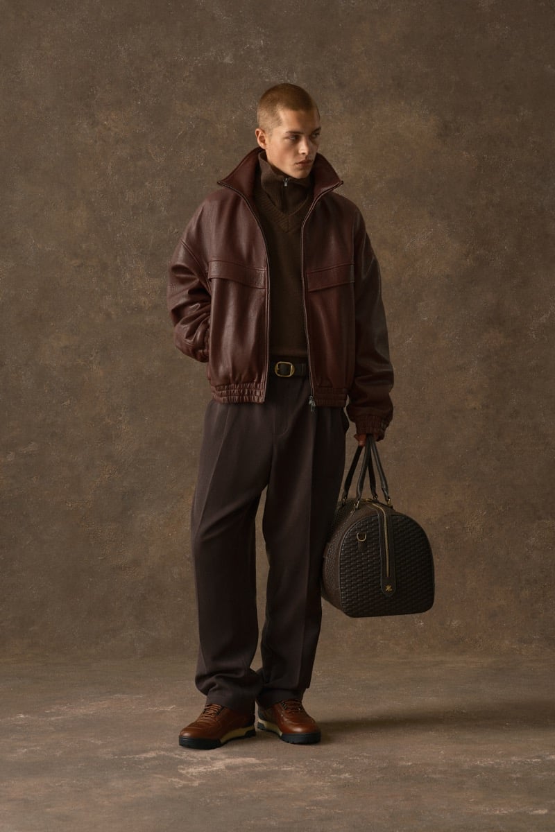 Man in a burgundy leather jacket and brown turtleneck, carrying a woven duffel bag, for Kith Fall 2026