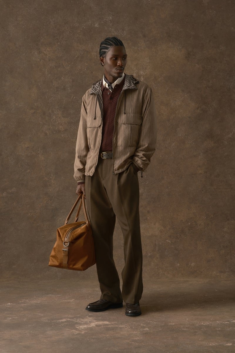 Man in a striped jacket with a zebra-print collar over a burgundy sweater, carrying a tan duffel bag, for Kith Fall 2026