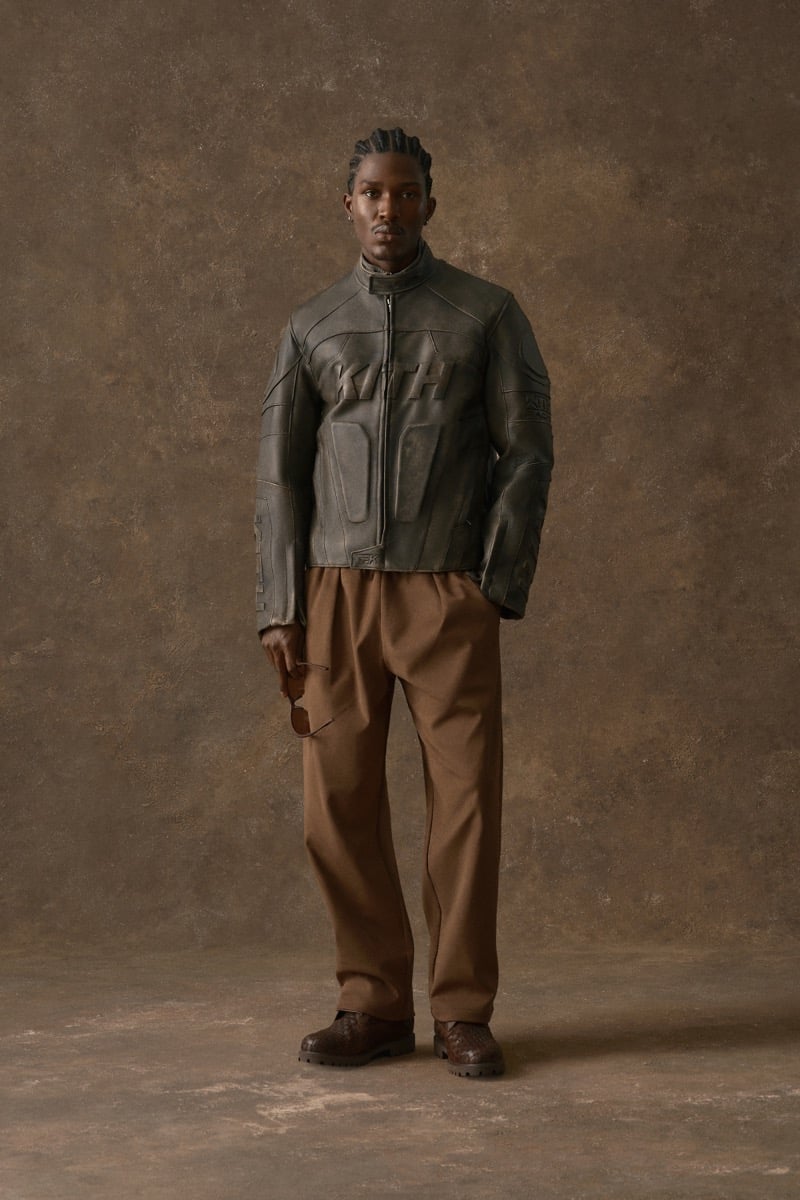 Man in an olive leather jacket embossed with the Kith logo, wearing camel trousers, for Kith Fall 2026
