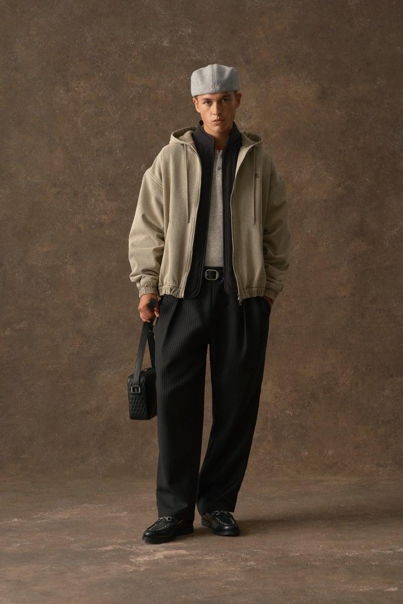 Man in a stone-colored hooded jacket, wearing a cap and black pinstripe trousers, for Kith Fall 2026