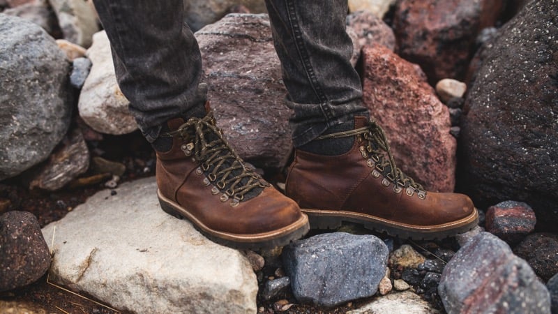 A close-up of brown leather lace-up hiking boots on a rocky riverbank