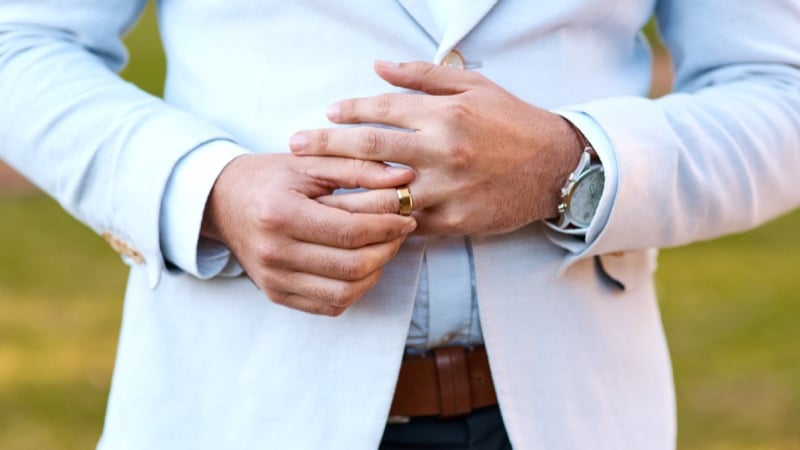 A man in a blue shirt adjusts a gold wedding band on his finger