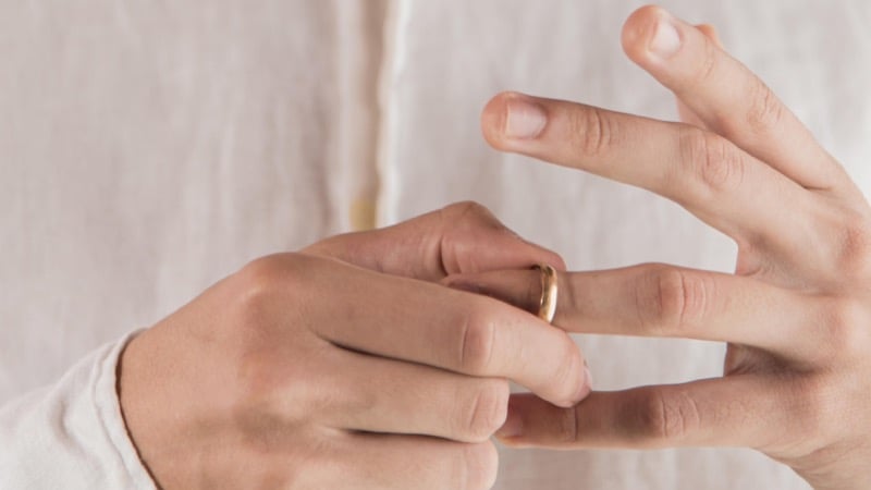 Close-up of a man in a white shirt pulling a gold wedding ring off his finger