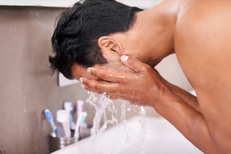 Man bent over a bathroom sink splashing water onto his face