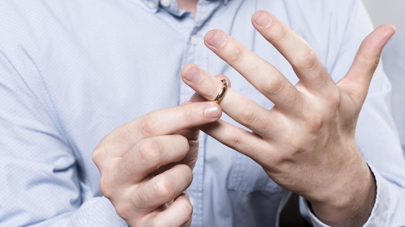 A man in a suit and watch takes off his gold wedding band