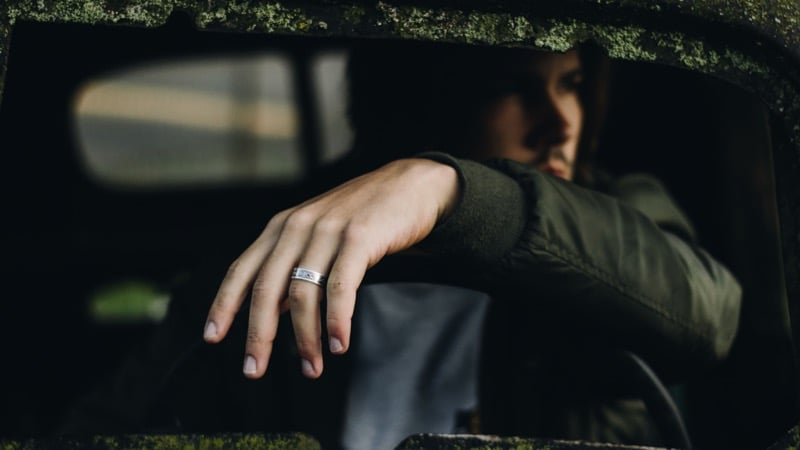 A man reaches his arm out of a car window, wedding ring visible on his hand