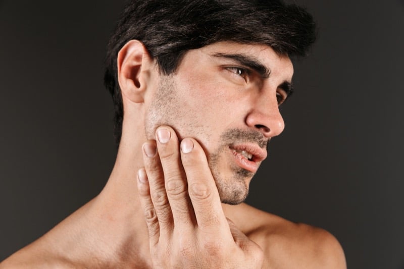 Shirtless man with stubble pressing a hand against his jaw and neck