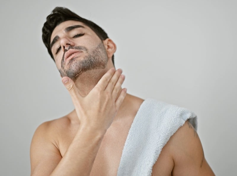 Man with a towel over one shoulder resting a hand on his freshly shaved neck
