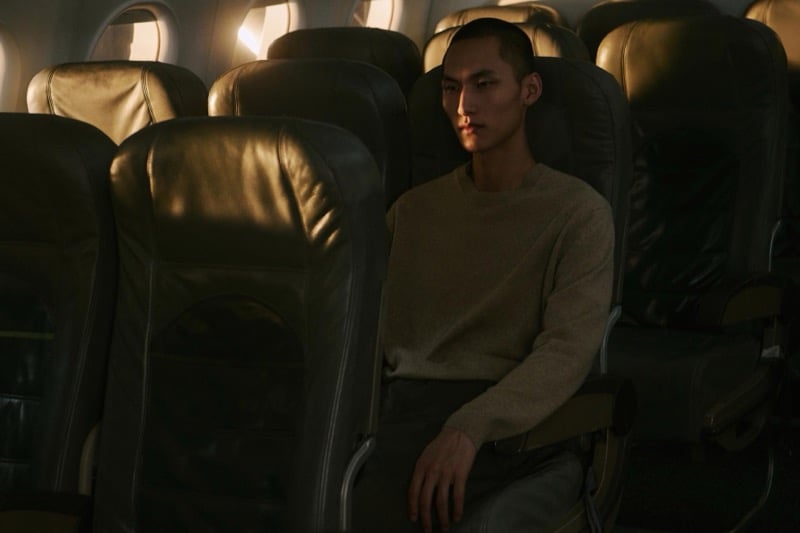Siquan Wang sits between airplane seats in a tan knit sweater