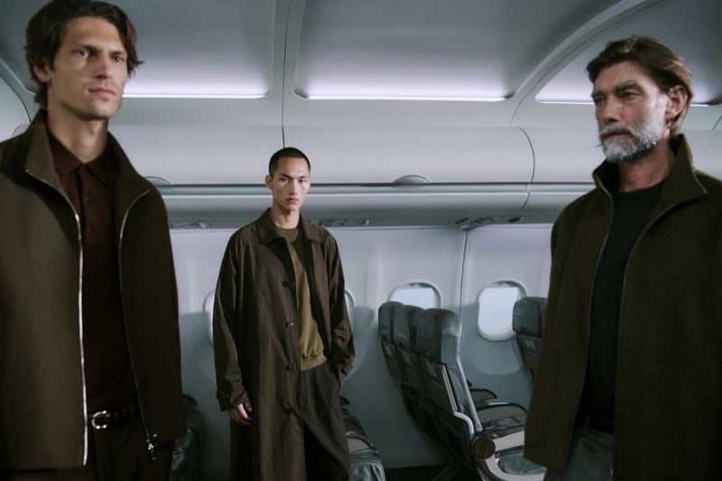 Justin, Siquan, and Patrick stand together in brown jackets and coats in the airplane aisle