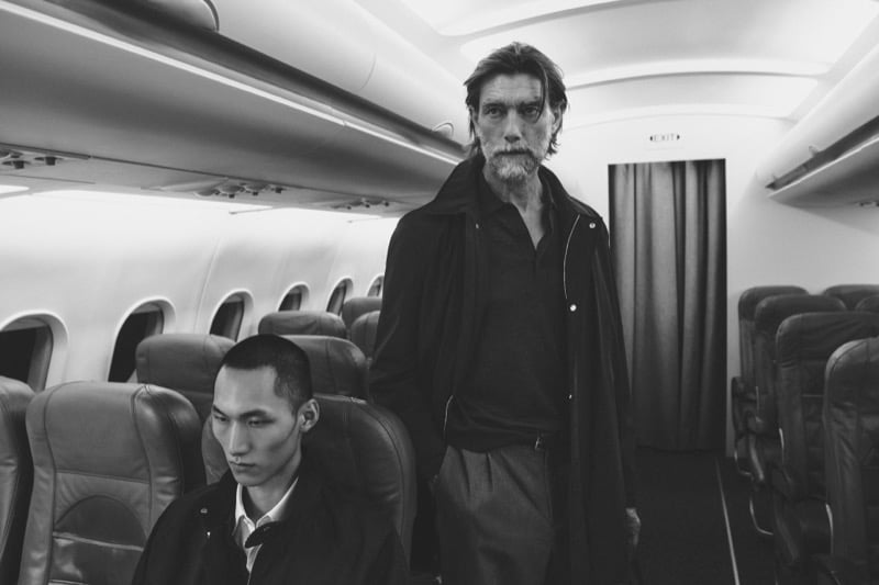A black-and-white image shows Patrick Petitjean standing behind a seated Siquan Wang inside the airplane cabin