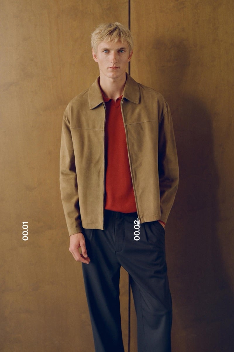 Pierrick Grégoire wears an open tan suede jacket over a rust polo with dark tailored trousers