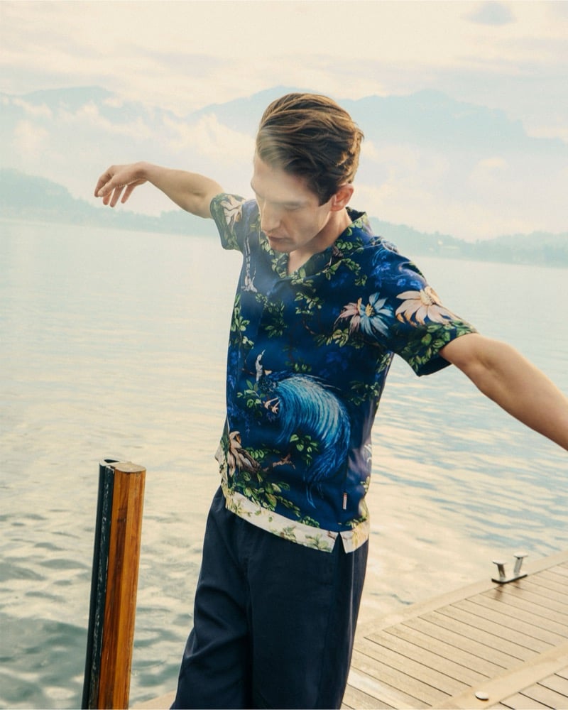 Anatol Modzelewski swings his arms on a lakeside dock wearing a botanical and toile-print camp-collar shirt