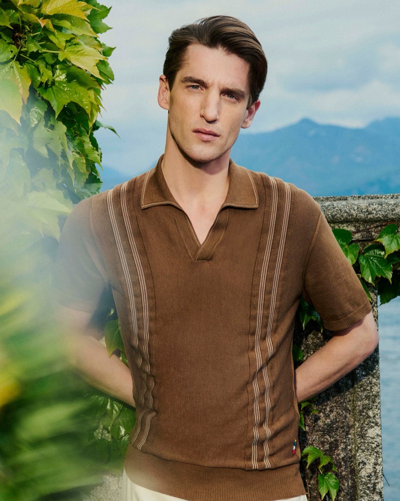 Anatol Modzelewski stands on a stone terrace wearing a brown textured knit polo with tan stripe detail