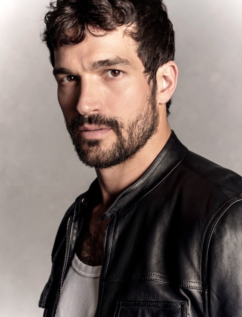 Paul Anthony Kelly in a close-up portrait wearing a black leather Prada jacket over a tank top