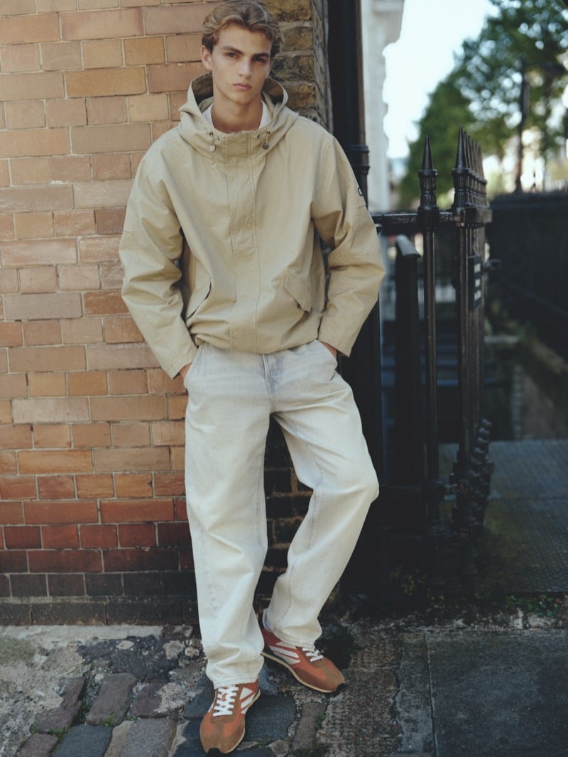 Maurits Scheij in a beige hooded jacket and pale jeans against a brick wall